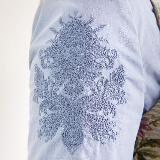 Blaue textile Oberfläche mit aufgesticktem, ornamentalen Muster in hellblau.