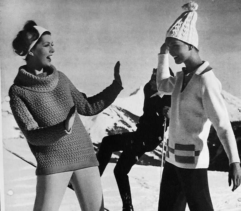 Zwei fröhliche Skifahrer in modischer Winterbekleidung posieren vor einer verschneiten Gebirgslandschaft.