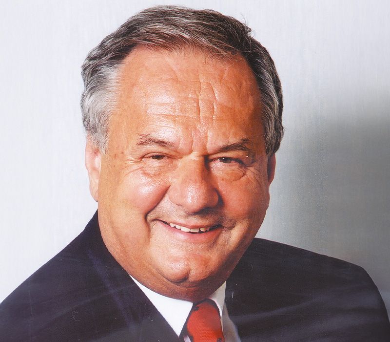 Ein lächelnder Mann mit grauen Haaren und einem Anzug, der in die Kamera schaut.