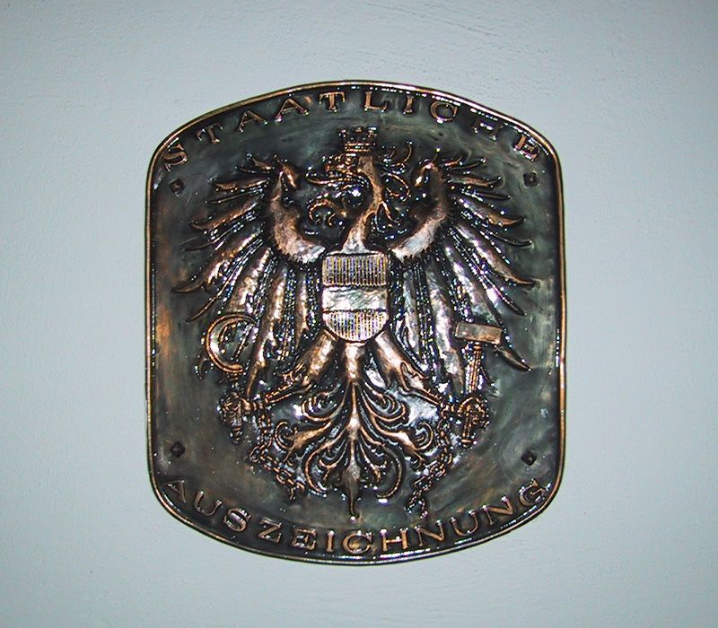 Ein goldenes Wappen mit dem deutschen Bundesadler und der Aufschrift "STAATLICH AUSZEICHNUNG".