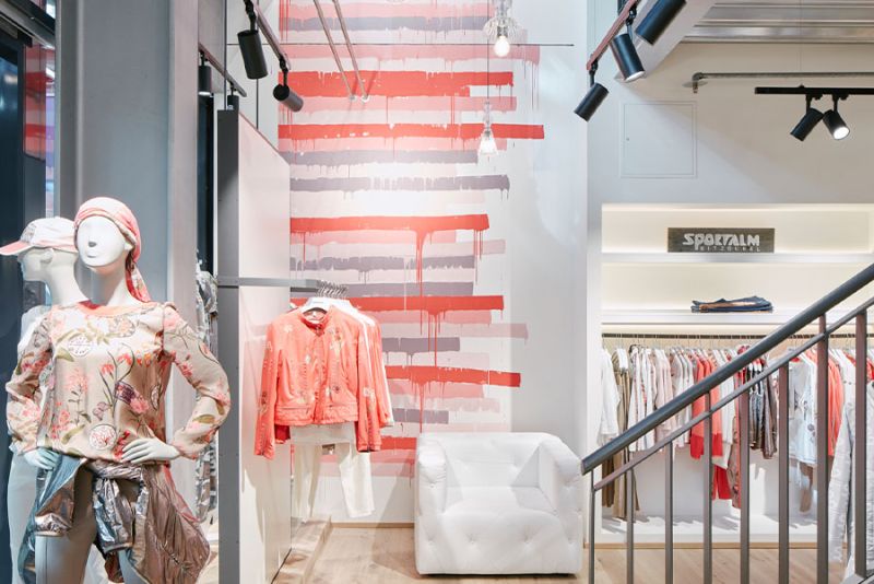Ein moderner Bekleidungsraum mit mannequins, bunt gefärbter Wand und einer Kleiderstange mit verschiedenen Kleidungsstücken.