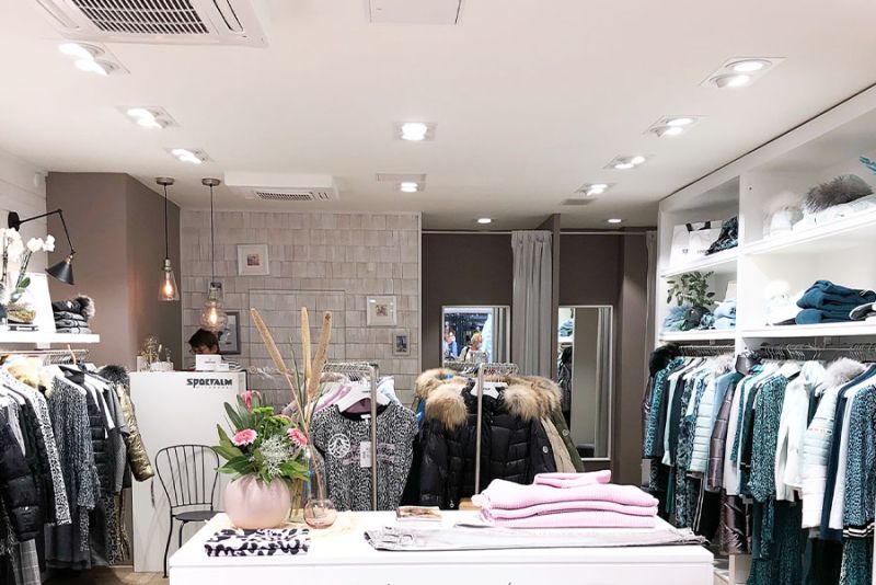 Modegeschäft mit einer Auswahl an Damenoberbekleidung und Accessoires, beleuchtet von Deckenleuchten.
