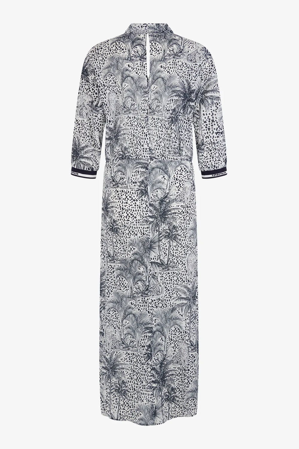 Eine Frau trägt ein gemustertes Kleid und hält einen gestreiften Schal in der Hand, während sie im Freien steht und der Wind durch ihr Haar weht.