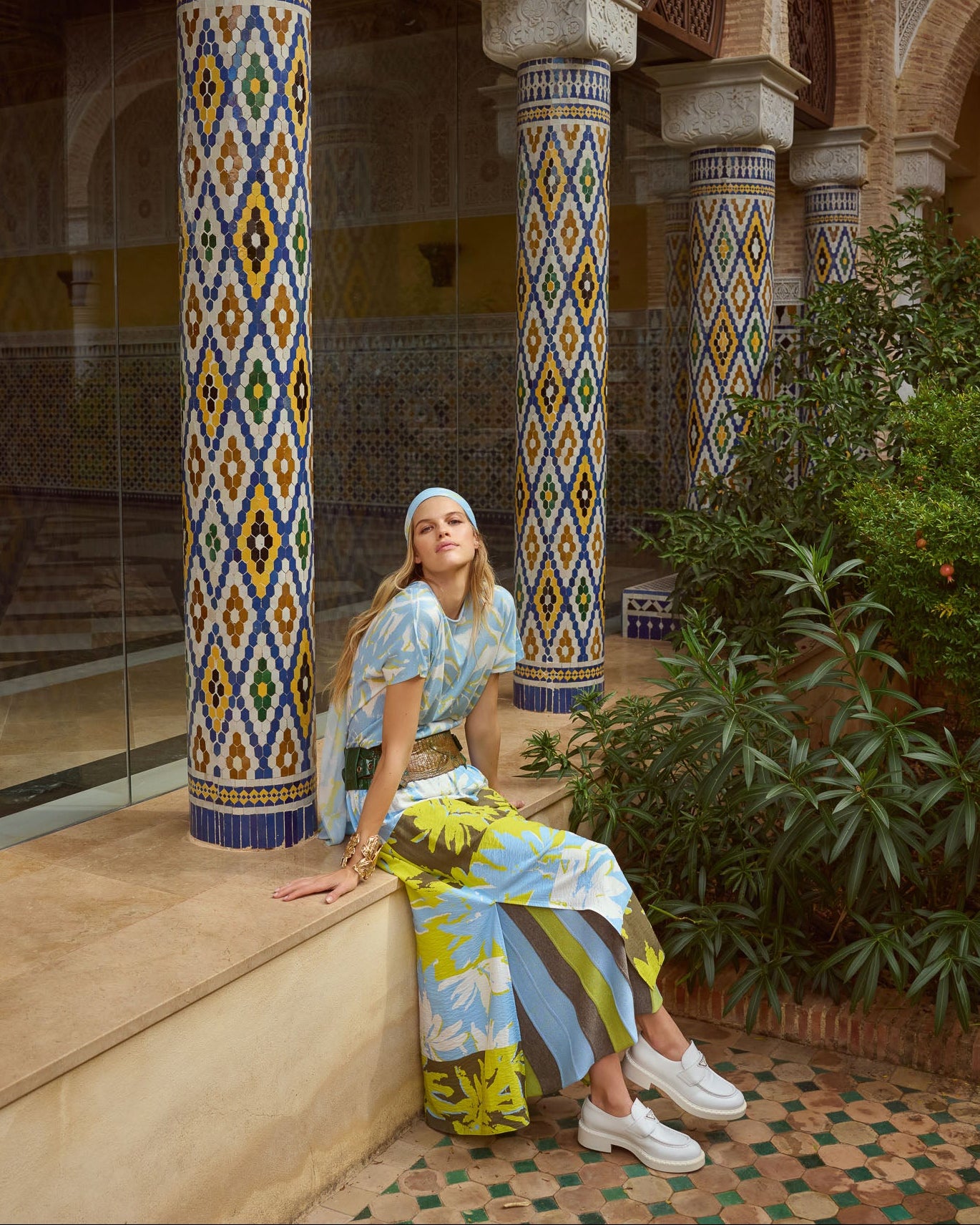 Frau in farbenfrohem Outfit von Sportalm vor kunstvoll verzierten Säulen in mediterraner Architektur.