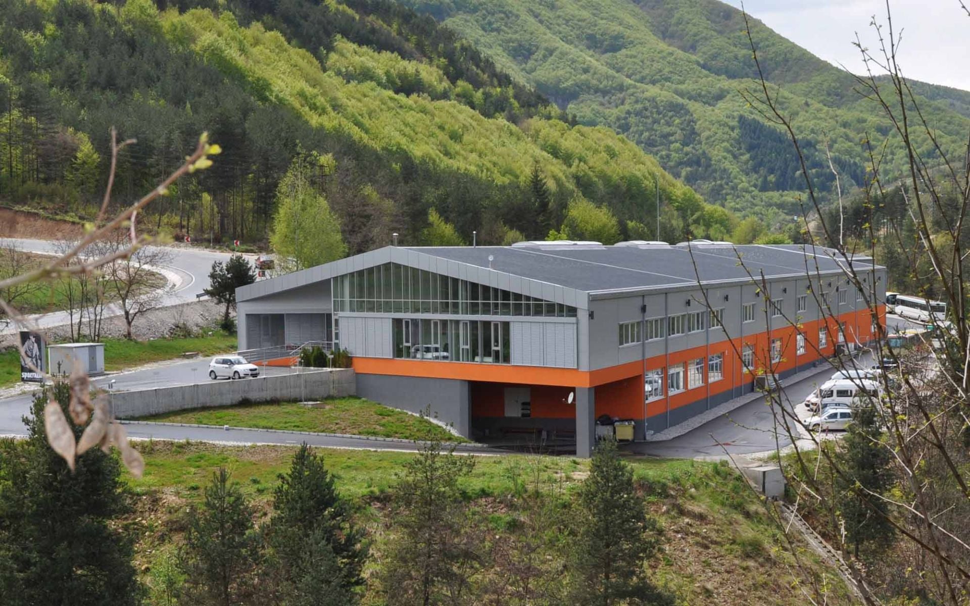 Modernes Industriegebäude mit orangefarbenen Akzenten in einer grünen Hügel-Landschaft.