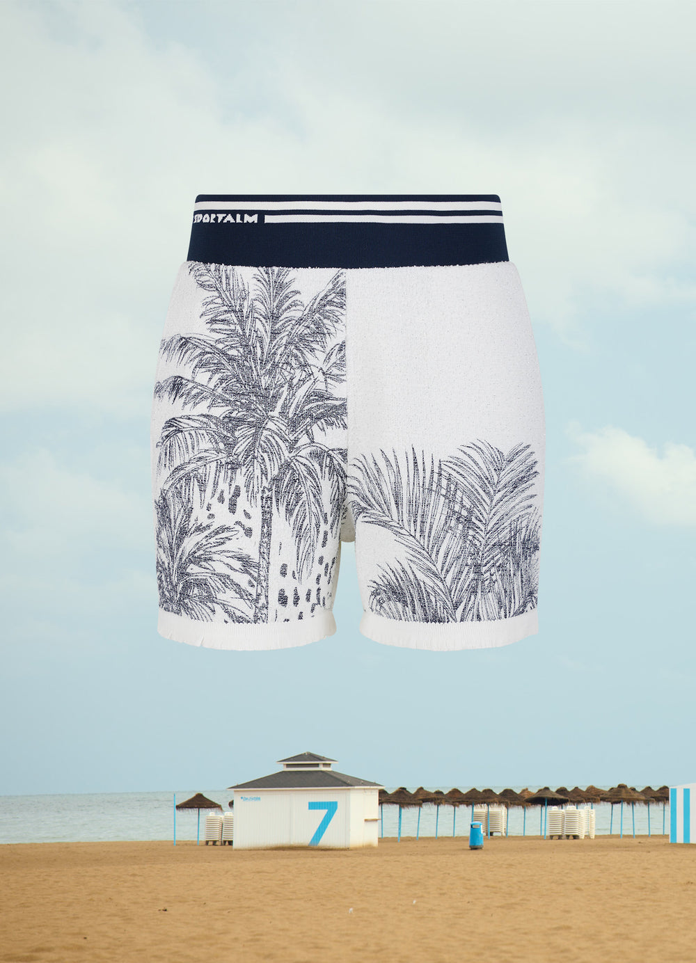 Kurze Badehose mit Palmenmotiv vor einer Strandkulisse.