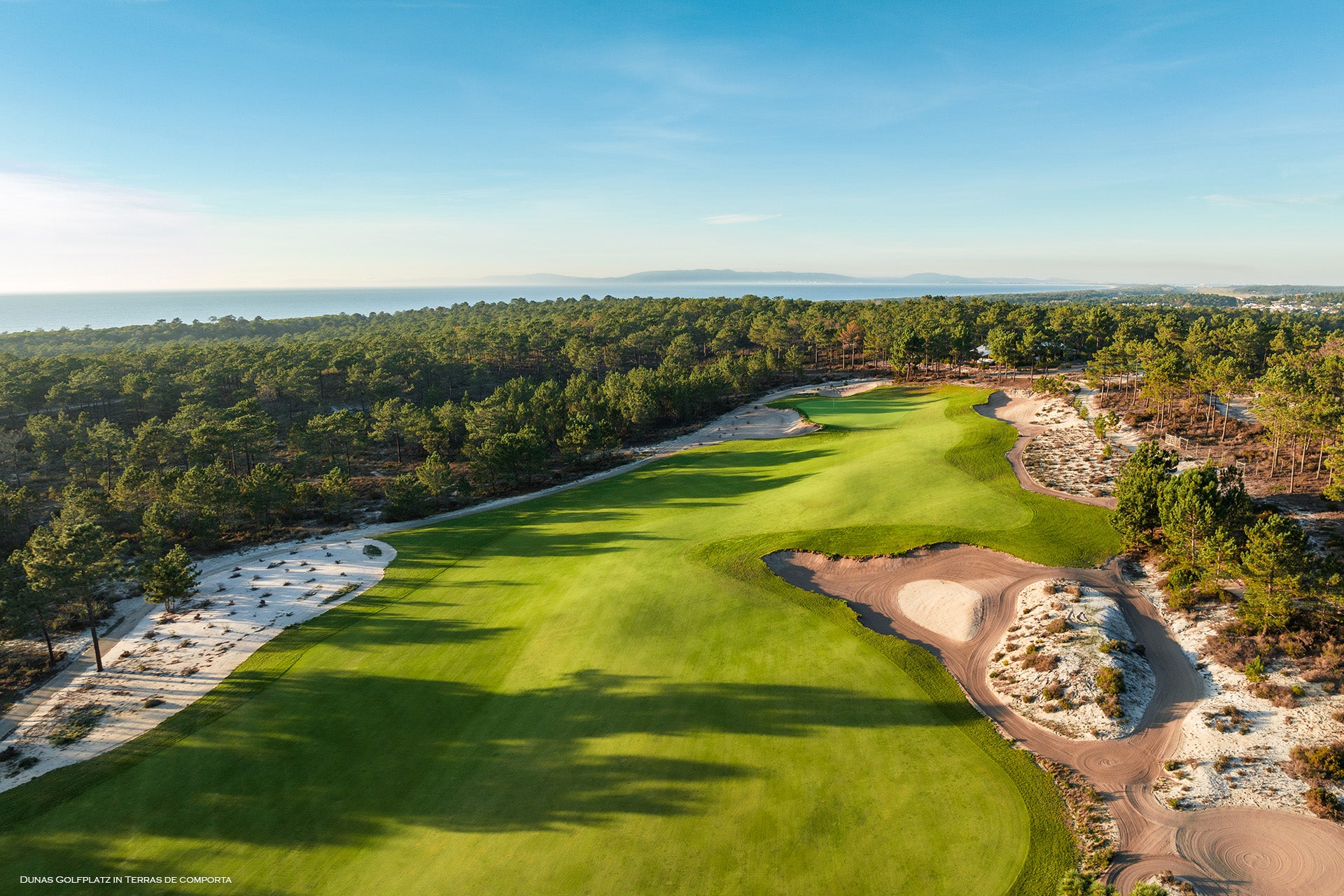 Ein weitläufiger Golfplatz mit sanften Hügeln, Bäumen und Sandbunkern unter blauem Himmel.