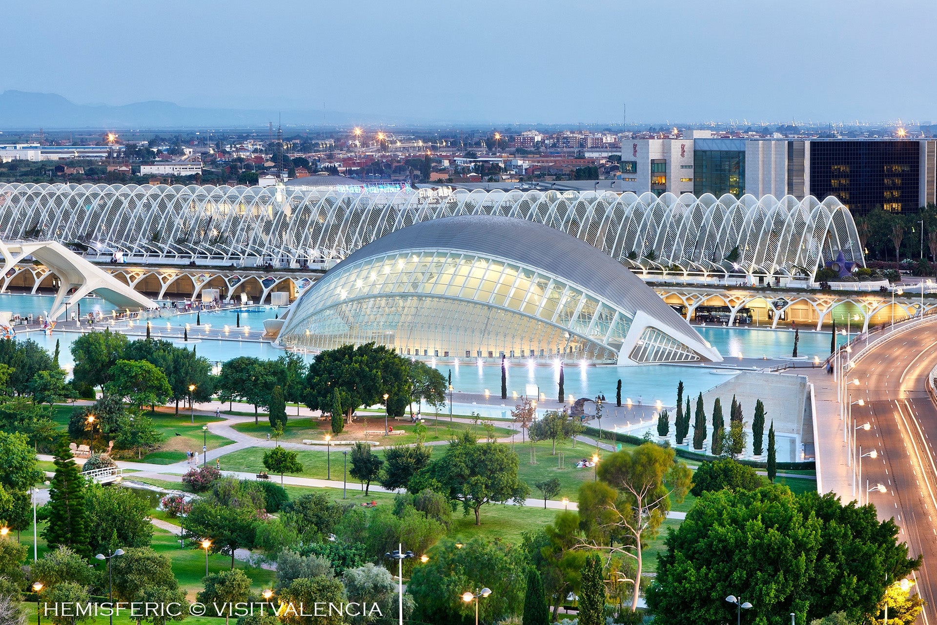 Moderne Architektur des Hemisférico in Valencia, umgeben von Wasser und Grünanlagen, bei Dämmerung.