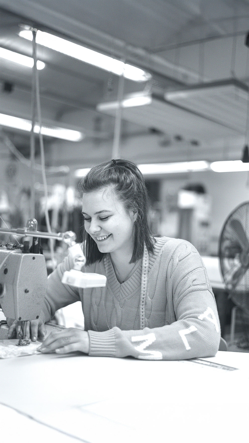 Eine junge Frau mit Zopf, die an einer Nähmaschine in einem hellen Atelier arbeitet.