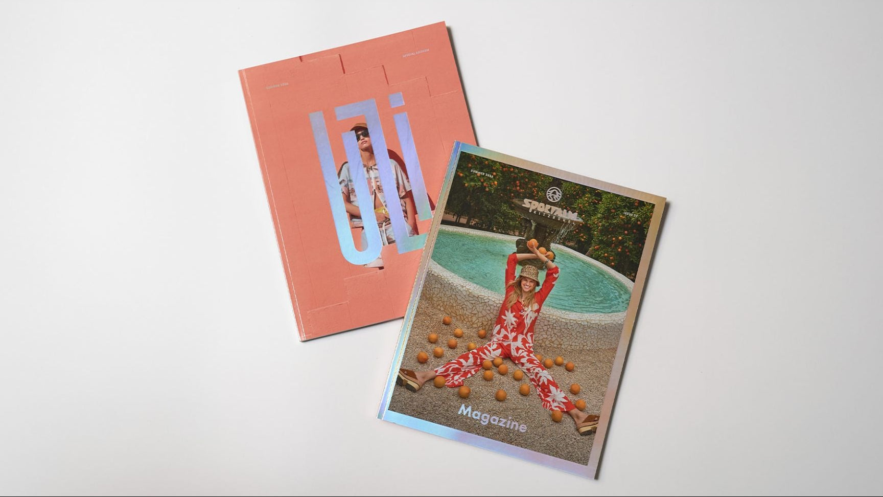 Zwei Magazine liegen nebeneinander auf einem weißen Untergrund, eines mit einem roten Cover und einem glänzenden Hintergrund, das andere mit einem Bild von einer Person in einem bunten Outfit am Rand eines Pools.