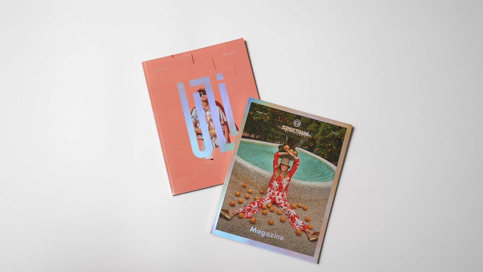 Zwei Magazine liegen auf einem weißen Tisch, eines mit einem rosafarbenen Cover und das andere mit einem glänzenden Cover und einer Person am Pool.