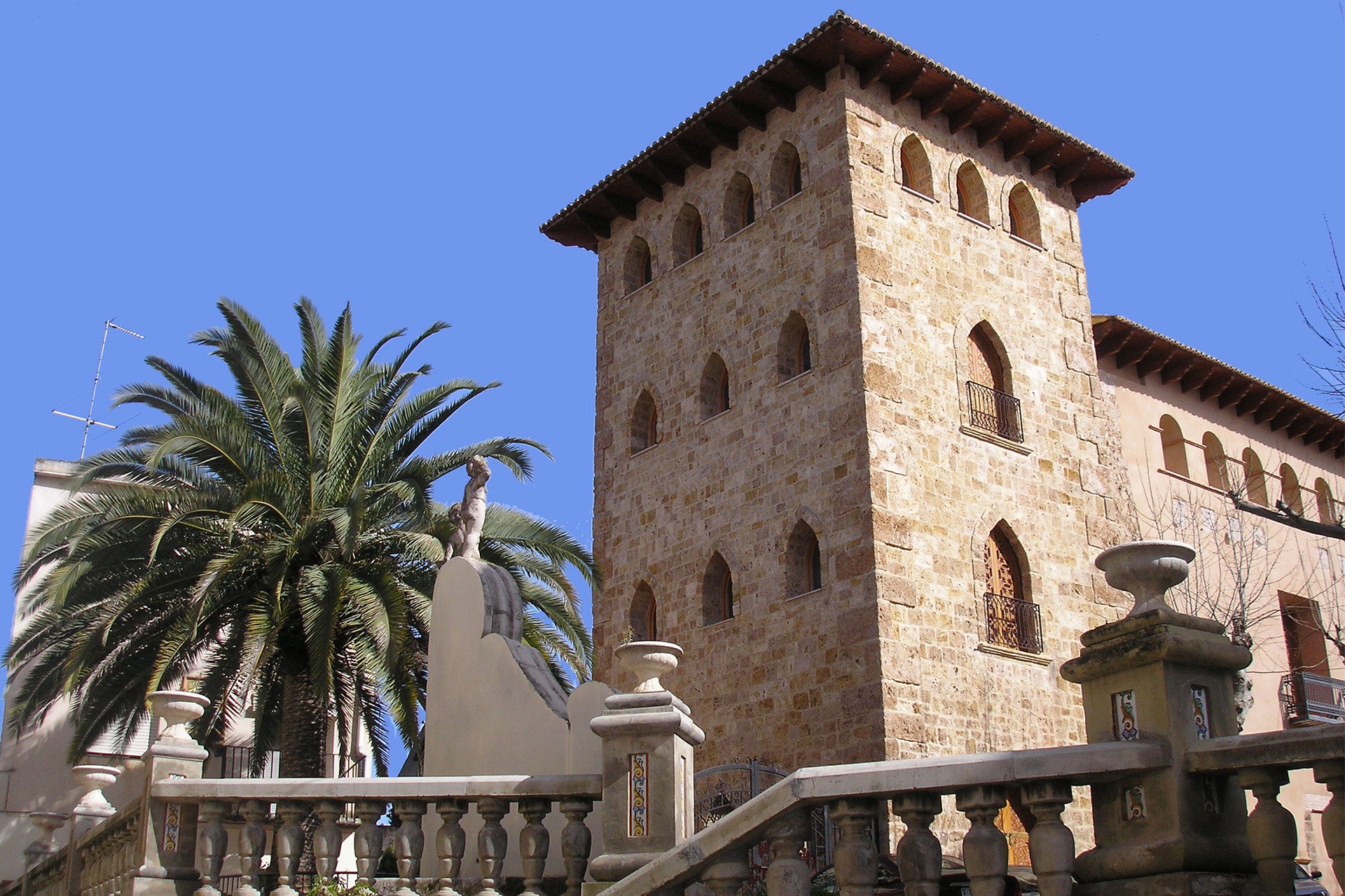 Historisches Gebäude mit Steinfassade, mehreren Fenstern und einem Palmenbaum im Vordergrund.