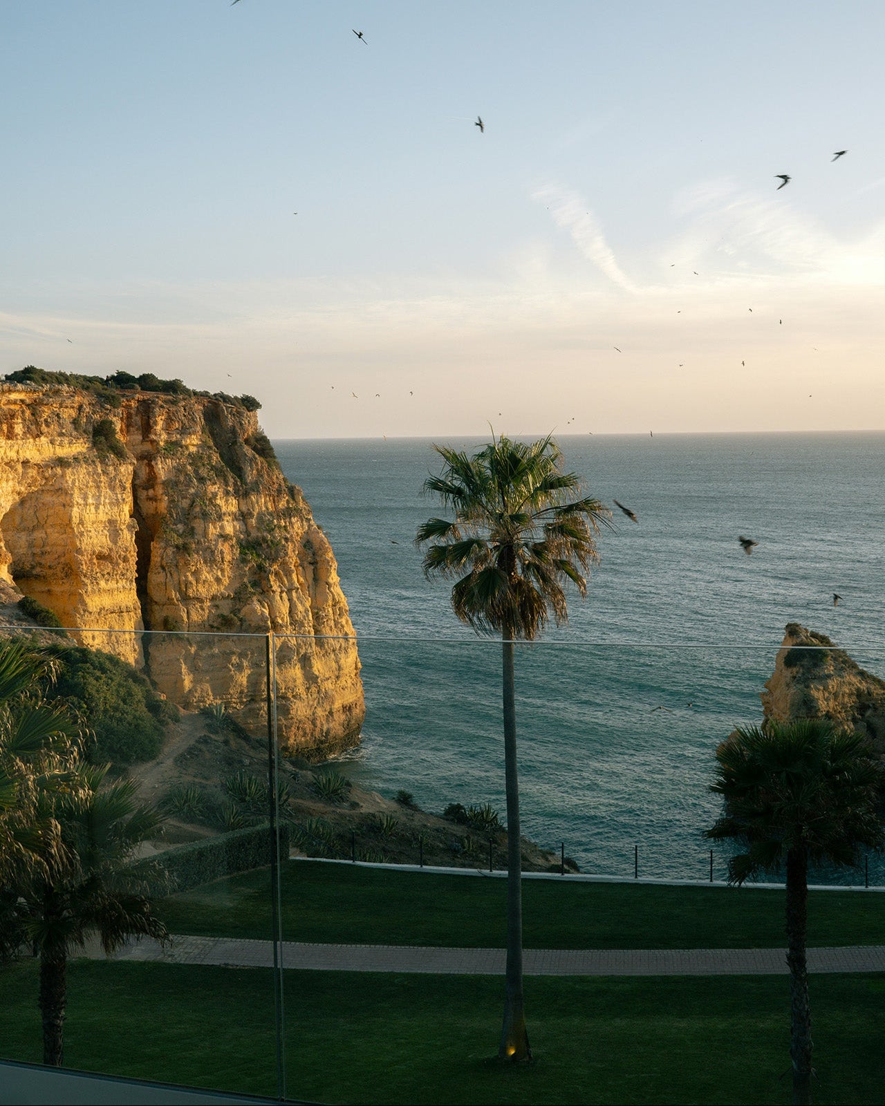 Küstenlandschaft mit hohen Felsen und Palmen, Blick auf das Meer bei Sonnenuntergang.