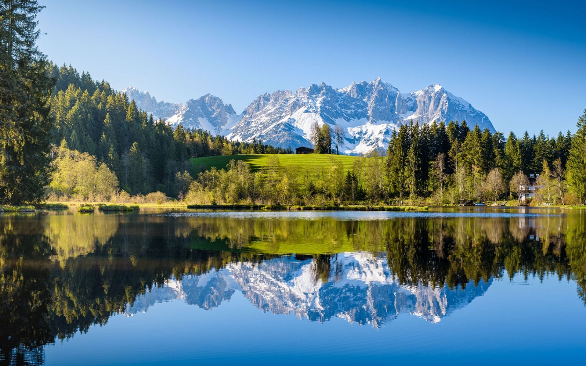 Idyllische Landschaft mit Berggipfeln im Hintergrund, einem klaren See und umgebenden Wäldern.