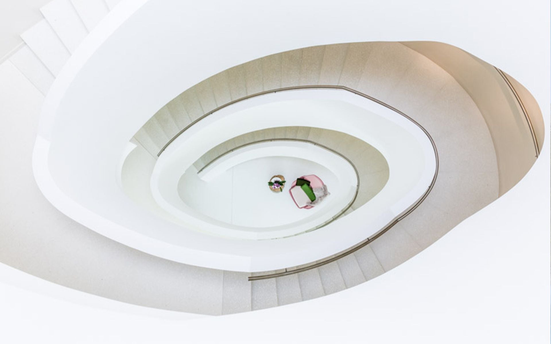 Eine spiralförmige Treppe mit hellem, minimalistischem Design und einer Person, die auf einer Sitzgelegenheit im Zentrum sitzt.