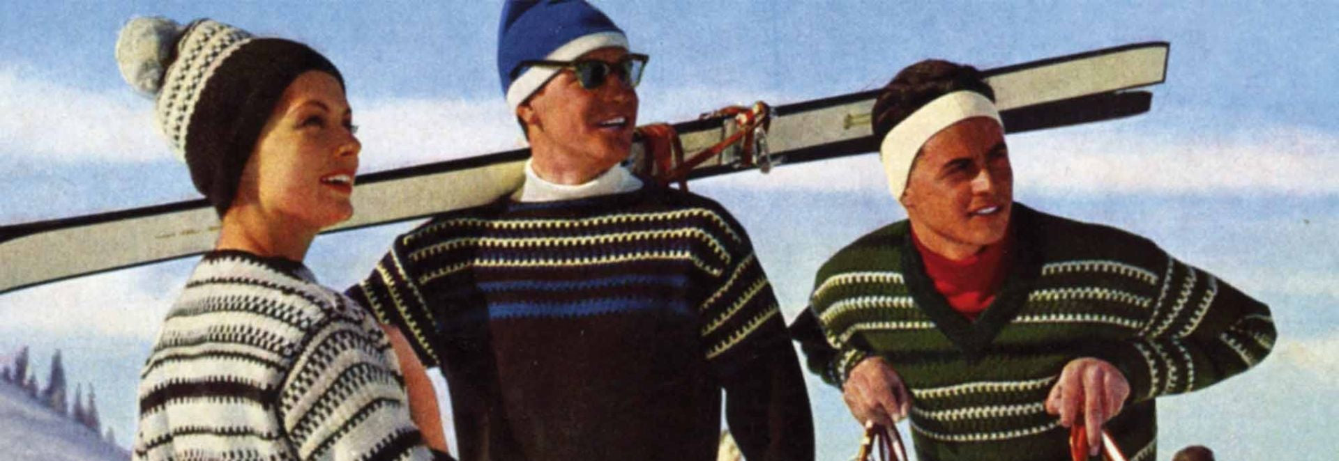 Drei Personen in winterlicher Skibekleidung stehen im Schnee, zwei mit Skiern über der Schulter und einer trägt einen blauen Hut.